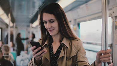 Caucasian woman using smartphone in subway car. Beautiful happy young office worker reading news from mobile app. 5G. 4K
