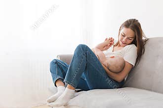 Mother breastfeeding baby sitting sofa home