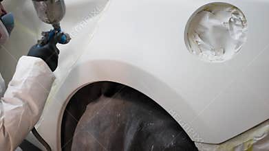 Close up shot of a worker slowly and caferully sparying paint with a gun all over car parts.