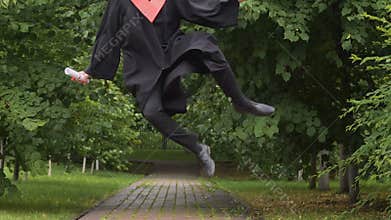 Smiling young man in academic dress walking and jumping, way to future success