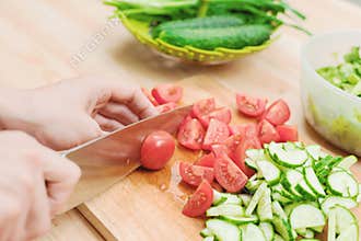 Close-up Delicate female hands cut a large knife with tomatoes on a quarter on a wooden board at home. Home kitchen
