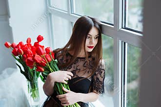 Portrait of young beautiful woman in black dress with tulips in luxury interior.