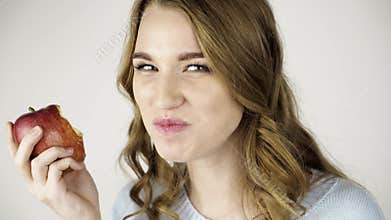 Fair haired woman biting a red apple and flirting close up
