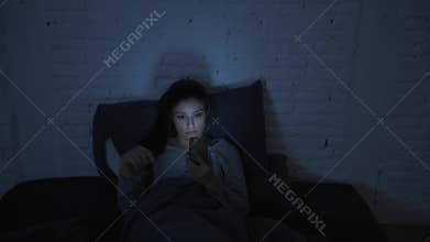 Frontal shot of young attractive hispanic woman on her 30s lying in bed late night using mobile phone look