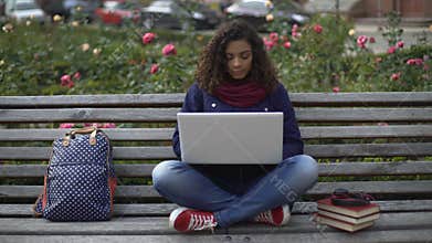 Young female student sitting on bench outdoors full-absorbed in the study