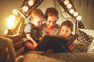 Happy family mother and children reading a book in tent at hom