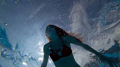 Beautiful girl with open eyes float underwater at clear blue swimming-pool on background bubbles