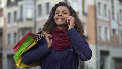 Woman with shopping bags calling female friends to tell about discounts in shops
