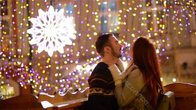 Romantic Couple with the Caucasian Appearance Kissing and Cuddling. Lights and Fireworks are On Background. Young Couple