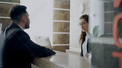 Receptionist girl talking with arrived businessman about check-in at reception in hotel. Business, travel and people