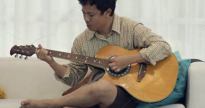 Asian man playing on a classical guitar.