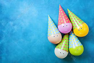 Funny colorful balloons in caps on blue table top view. Creative concept for birthday background. Flat lay.