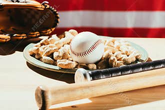 close-up view of baseball bats, baseball ball on plate with peanuts and leather glove on wooden table with us