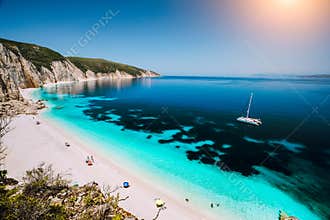 Fteri beach, Cephalonia Kefalonia, Greece. White catamaran yacht in clear blue sea water. Tourists on sandy beach near