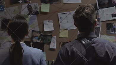 Two detectives examining and analyzing links between crimes looking at board