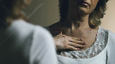 Senior woman looking at her reflection, upset with aging and sagging skin