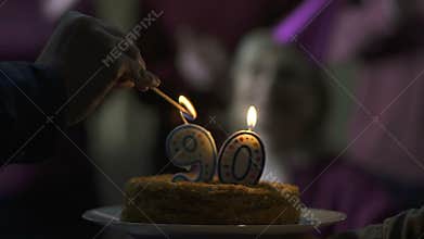 Male hand lighting candles on cake for 90 years old mother birthday, family care