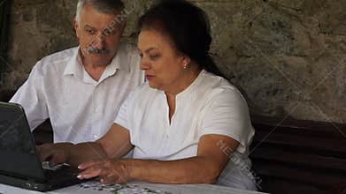 Adult senior couple with laptop at courtyard