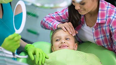 Adorable child smiling after dental procedures, watching healthy teeth in mirror