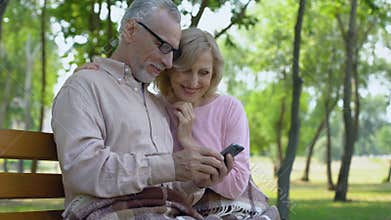 Grandfather and grandmother admiring children photos in smartphone application