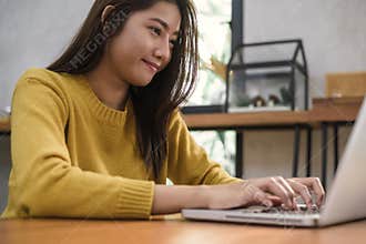 Young asian woman working with the laptop on a desk with her smile.