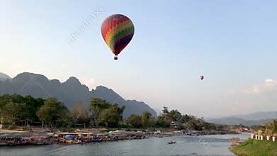 A large colorful balloon flies over the river in Laos.