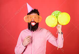Hipster in giant sunglasses celebrating. Guy in party hat with air balloons celebrates. Man with beard on cheerful face