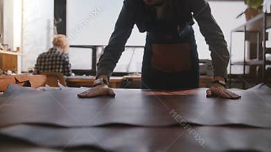 Close-up view of professional craftsman spreading a big piece of leather in modern manufacturing workshop slow motion.
