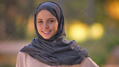 Close-up portrait of Muslim girl in hijab watching into camera, happily nodding to show agreement.