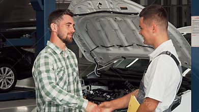 Cheerful man shaking hands with car mechanic at service shop