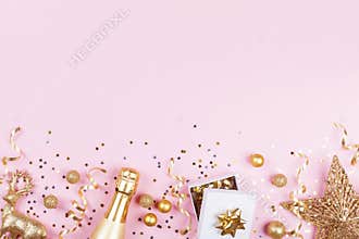 Christmas background with golden gift or present box, champagne and holiday decorations on pink pastel table top view. Flat lay.