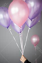 women's hand holding pink and purple helium balloons