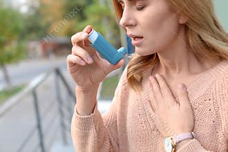 Woman using asthma inhaler outdoors, closeup