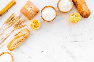 Farinaceous food. Fresh bread and raw pasta near flour in bowl and wheat ears on white stone background top view copy