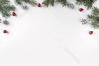 Creative frame made of Christmas fir branches on white background with red decoration, pine cones.