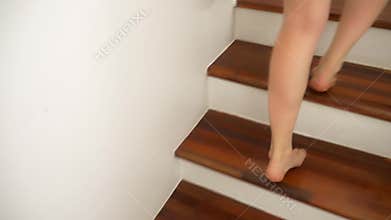 Close-up. The bare feet of a Caucasian woman climb to the top of the wooden stairs.