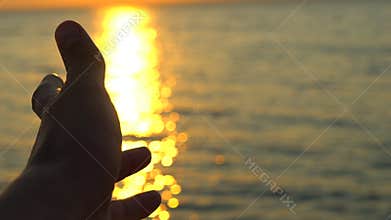 Man hand at sunset on sea, ocean beach. A man`s hand in sun`s rays on background sea water in nature. Glare of evening
