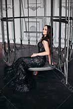 Beautiful brunette woman wearing shiny black dress posing in cage like bird.