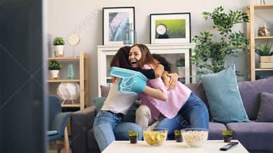 Girls watching sports at home cheering then laughing clapping hands hugging
