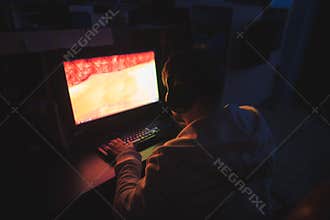 Focused gamer sits at the computer at home in the cozy room and plays horror games on the computer