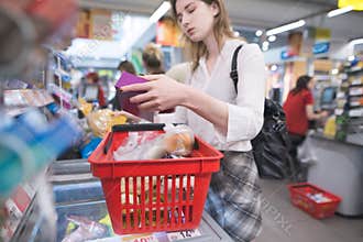 Woman stands at the supermarket`s cash register and discharges the goods out of the basket