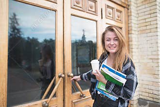 Smiling student girl what with books. Notebooks and a cup of coffee are on the inside of the door