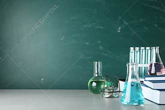 Laboratory equipment and books on table near chalkboard with space for text. Chemistry