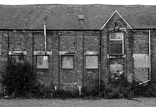 Old abandoned brick factory building with boarded up windows and crumbling decaying walls overgrown with weeds