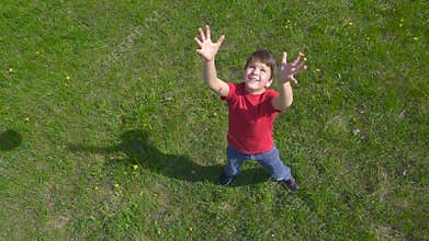 Boy throws up the ball, standing on green lawn