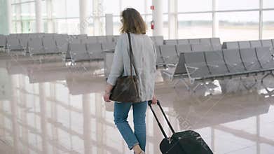 Ginger red hair woman girl at airport walking with rolling luggage suitcase bag