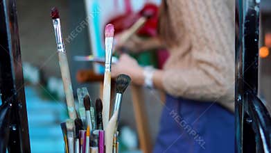 Close up shot of dirty brushes, in the background a woman paints a picture
