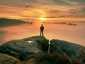 Man stands alone on the peak of rock. Hiker watching to autumn Sun at horizon . Beautiful moment the miracle of nature. Colorful