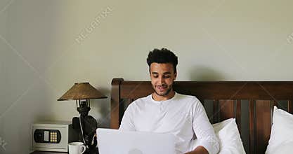 Pondering Man Using Laptop Computer Sitting On Bed Hispanic Guy Type Chatting Online In Bedroom Morning