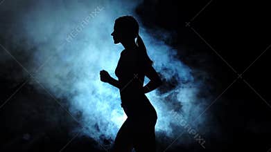 Lady running on a smoky spotlight on black background. Silhouette. Slow motion